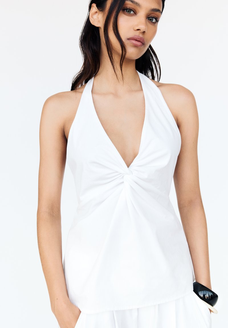 Top bianco con scollo a V profondo e dettaglio frontale attorcigliato. Realizzato in tessuto leggero con una consistenza liscia e silhouette aderente.