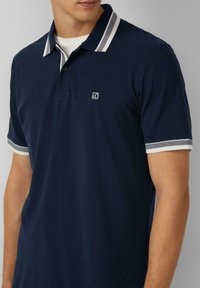 Marineblauwe polo, kenmerkt zich door een contrasterende witte gestreepte kraag en mouwboorden, korte mouwen en een klein logo op de borst.