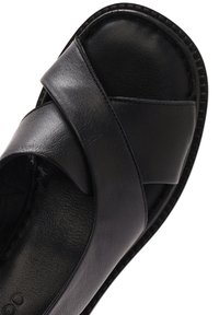 Sandale noire avec un design à bride croisée, fabriquée en cuir lisse. Caractéristiques : bout arrondi et semelle texturée avec des coutures visibles.