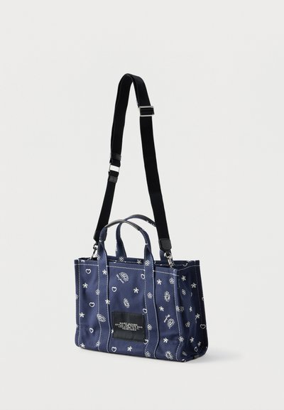 Granatowa torba na ramię z białymi nadrukami w gwiazdki, serca i kwiaty, czarnym regulowanym paskiem na ramię oraz przednią etykietą z napisem.
