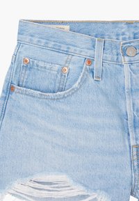 Shorts de mezclilla en azul claro con dobladillo deshilachado, detalles en tono cobre y diseño de cinco bolsillos. Cuenta con un cierre clásico de botón y cremallera.