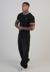 Mustade lühikeste varrukatega t-särk, kontrastsete äärtega, sobib kleidi disainiga, kombineeritud lahtiste mustade pükste ja hallide aktsentidega valgete Sneakeritega.