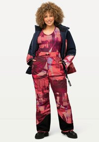 Tenue d'hiver extérieure comprenant une veste rembourrée et un pantalon dans des nuances de rose et de bordeaux avec des motifs abstraits, accompagnés de bottes noires robustes.