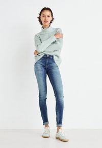 Mintgrønn stripet høyhalset genser med oversized passform, sammen med mørkeblå skinny jeans og lyse sneakers med hvit såle.