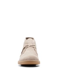 Beige mockasklätterskor med snörning, rund tå, en enkel design och en ljusbrun gummisula. Har minimala sömmar och hål för snören.