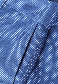 Tela azul con pequeños lunares blancos, que presenta una textura suave y un borde doblado, destacando un diseño limpio y a medida.