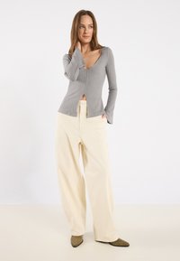 Gray ribbed long-sleeve top with a V-neck and front slit, paired with cream wide-leg pants and green pointed-toe shoes.