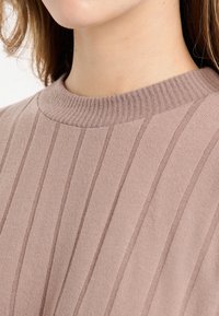 Jasnoróżowy sweter o pionowej prążkowanej fakturze i szerokim prążkowanym dekolcie. Materiał wydaje się miękki i gładki, podkreślając uporządkowany krój.