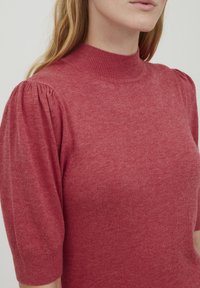 Röd tröja med hög hals, korta puffärmar och mjukt material. Har ett subtilt melerat mönster genom hela.