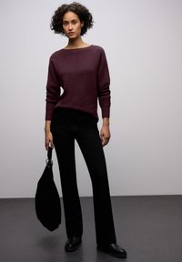 Maglione bordeaux lavorato a maglia con scollo rotondo, polsini a coste, abbinato a pantaloni neri a gamba dritta. Borsa nera con tracolla e dettagli in argento.