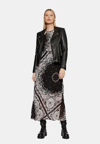 Giacca da biker nera in pelle sopra un vestito maxi a fantasia con design paisley bianco e rosa, completato da stivali combat neri.