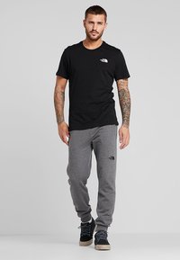 Sort bomulds T-shirt med et lille hvidt logo på brystet, parret med grå sweatpants med et sort logo og mørke sko.