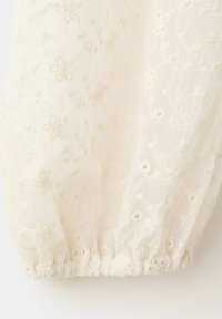 Tissu blanc transparent avec délicate broderie florale et ourlet élastique froncé, montrant la texture et les détails légers.