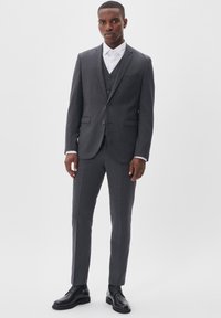 Traje de tres piezas gris oscuro con un patrón de cuadros fino, solapas con muesca y corte ajustado. Acompañado de una camisa de vestir blanca y zapatos negros de cordones.