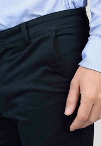 Pantalon noir avec une texture lisse et un design ajusté, doté de poches latérales. La taille est plate et sans couture pour une finition nette.