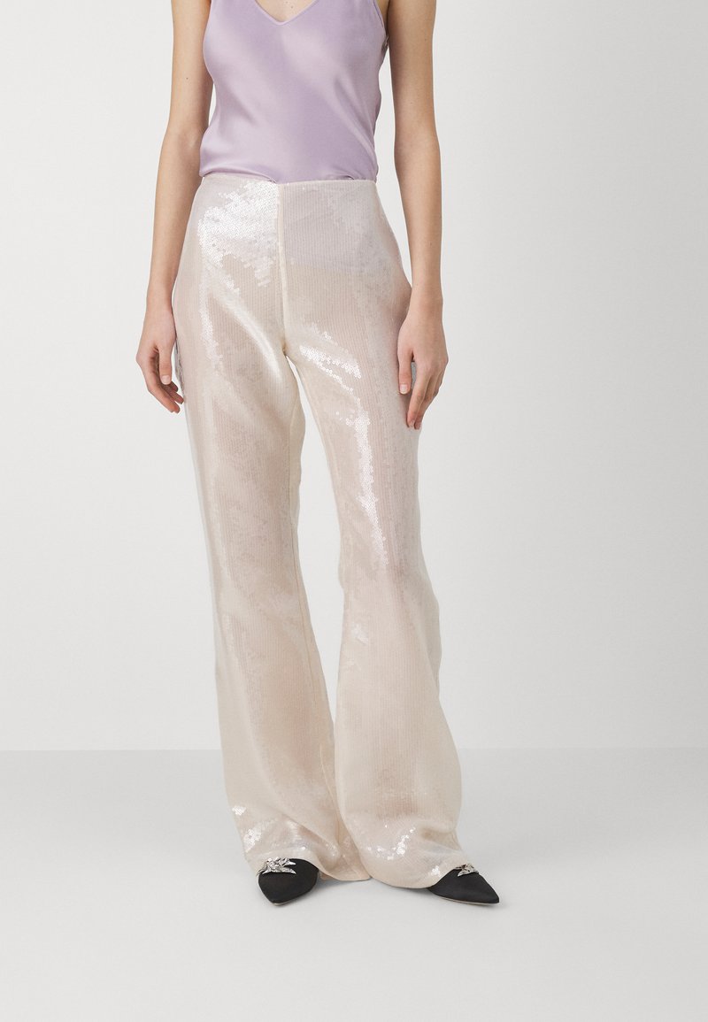 Pantaloni a zampa in crema trasparenti e con paillettes abbinati a un top senza maniche di colore lilla chiaro. Scarpe nere con punta a stiletto e dettagli argentati completano l'outfit.