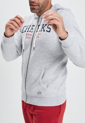 Sudadera de cremallera en gris claro con cordones, bolsillos frontales y texto impreso en rojo. Textura suave, con puños y dobladillo acanalados.