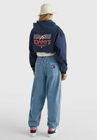 Sudadera corta de color marina con gráficos rojos y blancos en la parte posterior, combinada con jeans de mezclilla azul claro de corte relajado y zapatillas blancas con detalles en rosa.