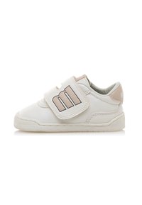 Zapatilla blanca con un acabado de cuero texturizado y una correa de velcro beige que presenta un logo. Suela de goma con un patrón de relieve mínimo.