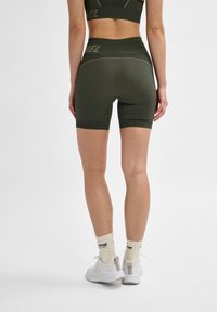 Prążkowane, oliwkowozielone spodenki sportowe z wysokim stanem i kontrastowymi szwami, w zestawieniu z białymi trampkami i kremowymi skarpetkami.