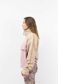 Beige en roze fleece pullover met een hoge kraag, voorzien van een vozak en logo-detail. Gepaard met gestreepte leggings in gedempte kleuren.