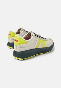 Sneakers in tela beige chiaro con una spessa suola blu scuro, dettagli giallo brillante e lacci neri. Logo "CAMper" visibile sul tallone.