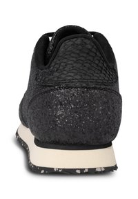 Talons de baskets noirs texturés avec une semelle intermédiaire blanche et une semelle extérieure noire à motifs sur fond blanc.