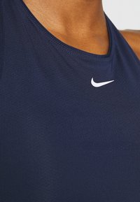 Marinblå atletisk linne med en slät, strukturerad yta och en vit Nike swoosh-logga på bröstet. Har en rundad halsringning.