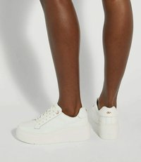 White platform sneakers made of canvas with a rounded toe, lace closure, and a textured rubber sole. Features gold-tone eyelets.