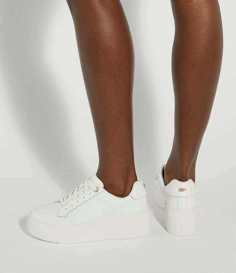 White platform sneakers made of canvas with a rounded toe, lace closure, and a textured rubber sole. Features gold-tone eyelets.
