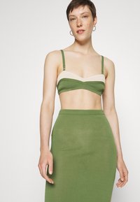 Bralette verde com texturas caneladas e detalhes em creme, com alças ajustáveis, emparelhado com uma saia midi verde justa, exibindo uma textura suave.