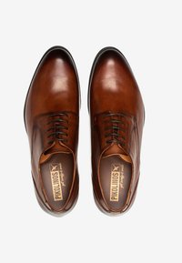 Chaussures habillées en cuir marron avec une finition lisse, dotées de cinq œillets et de lacets. Embout arrondi et détail de marque à l'intérieur visible.