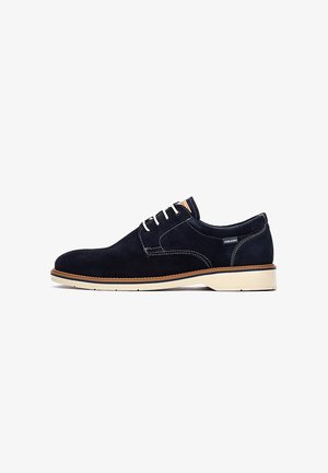 Chaussure pour homme en daim bleu marine à lacets, avec semelle blanche et garniture marron, présentée de profil sur fond blanc.