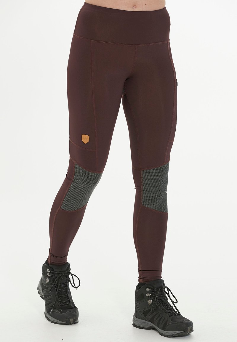 Leggings bordeaux avec des accents de panneaux gris, design taille haute, tissu extensible et un patch logo sur la cuisse. Des bottes de randonnée noires complètent le look.