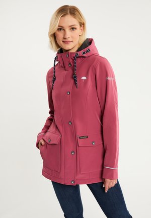 Donna con giacca impermeabile rosa con cappuccio e coulisse bianche e nere, tasche anteriori e jeans blu scuro su sfondo semplice.