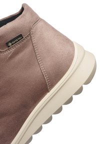 Zapato de ante marrón claro con suela gruesa blanca y etiqueta Gore-Tex en el lateral, que destaca el material impermeable y transpirable.