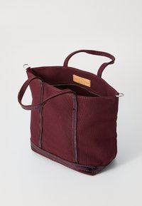 Bordový plátěný nákupní vak s dvoma krátkymi rúčkami, zosilneným šitím a zipsovým uzáverom. Vo vnútri má kožený štítok.