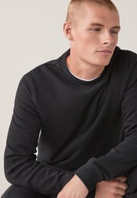 Czarny sweatshirt wykonany z miękkiego materiału, z okrągłym dekoltem, ściągaczami na rękawach i luźnym krojem. Posiada minimalne detale w stębnowaniu.