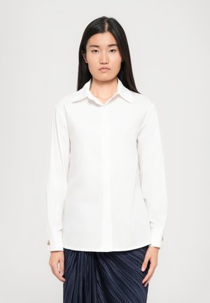 White long-sleeve shirt made of smooth fabric, featuring a classic collar, button closure, and gold accents on the cuffs.
