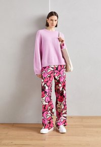 Ljusrosa stickad tröja med en avslappnad passform, kombinerad med vida blommiga byxor i rosa, beige och svart. Vita sneakers och en tote-väska.