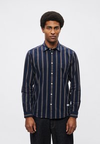 Granatowa koszula z długim rękawem w wielokolorowe pionowe paski, zapinana na guziki z przodu, z pojedynczą kieszenią na piersi oraz fakturą tkaniny ukazującą jej miękkość.
