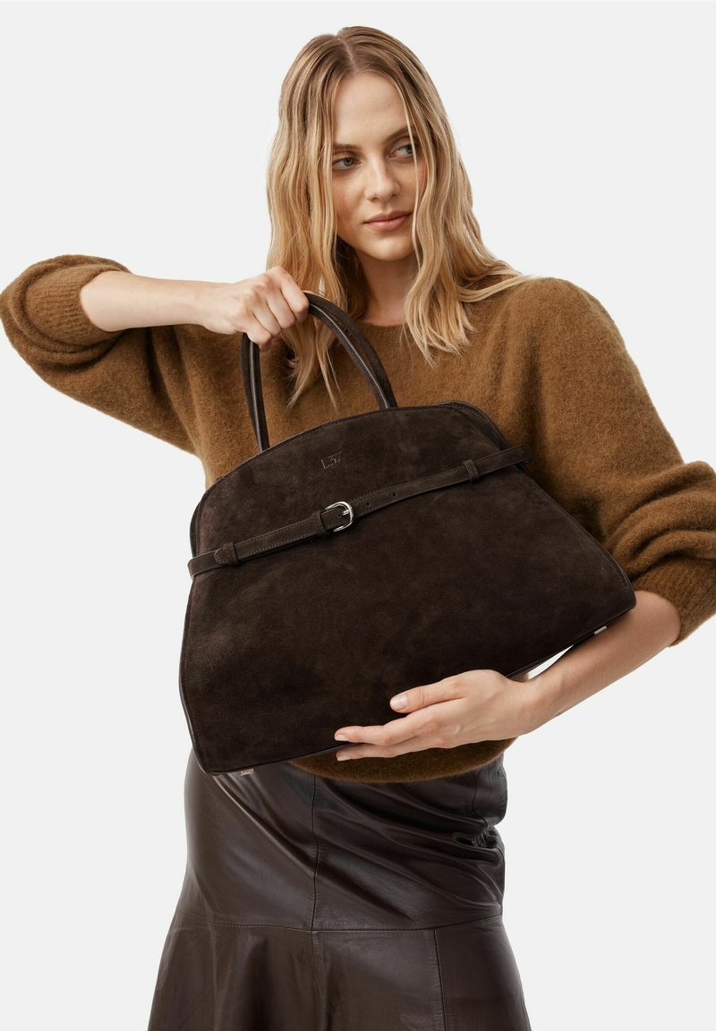 Borsa a tracolla in suede marrone scuro con forma strutturata, dotata di una tracolla in pelle e dettaglio con fibbia in metallo. Il modello tiene la borsa con due manici.