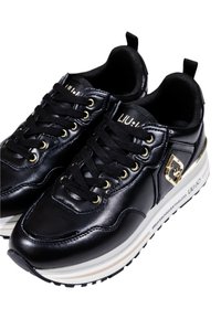 Sneakers neri con una finitura in pelle lucida, dotati di accessori in oro, lacci neri e una suola intermedia bianca con un audace dettaglio del logo.