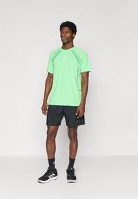 Green athletic t-shirt with black accents, paired with black shorts. Features a logo on the chest and a relaxed fit.