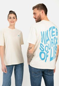 Cremfarbendes Baumwoll-T-Shirt mit einem blauen Grafikdruck auf der Rückseite, der "WASSERQUELLE DES LEBENS" sagt. Rundhalsausschnitt und kurze Ärmel.