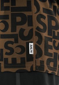 Braunes T-Shirt mit großem schwarzem "SLOPE"-Textmuster und einem kleinen weißen Etikett mit dem Markennamen. Weicher Stoff, lässiges Design.