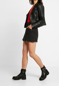 Giacca da motociclista in pelle nera con spalle testurizzate, top rosso, mini gonna in denim nera, e stivaletti neri con hardware e suola spessa.