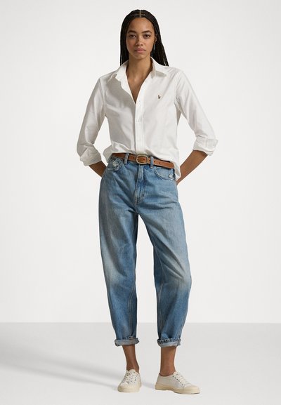 Hvit skjorte med knapper, lyseblå jeans med oppbrett, brun lærbelte, kremhvite sneakers; uformell passform, enkel design uten mønstre.