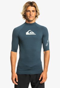 Short-sleeve rash guard in navy blue fabric, featuring a white logo on the chest and sleeve. Smooth texture, fitted design.