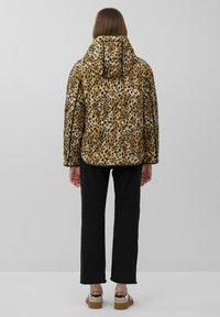 Gequilted jack met een luipaardprint in bruin- en zwarttinten; heeft een capuchon en zwarte details; gedragen met zwarte broek.